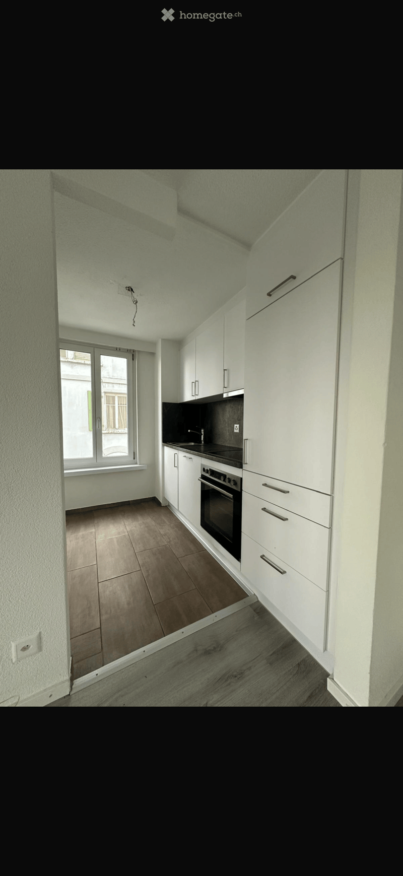 Modern kitchen with white cabinets, black countertop, and wooden flooring. Features an oven, sink, and ample storage space.