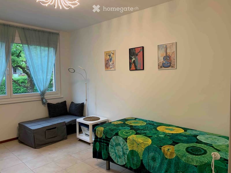 Cozy bedroom with a bed, sofa, small table, floor lamp, and artwork on the walls.