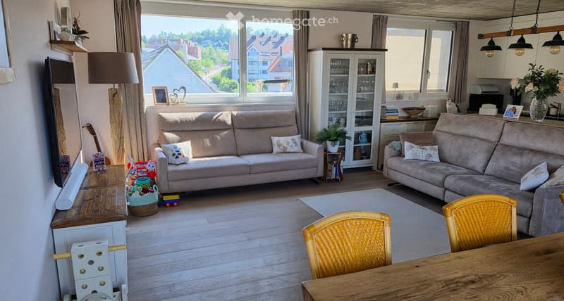 Bright living room with large windows, two sofas, a wooden dining table, and various decorative items including a guitar, a cat, and a vase with flowers.