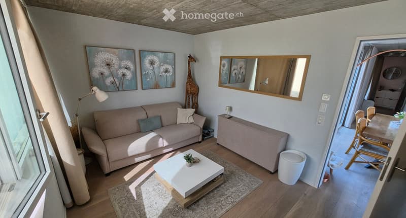 Bright living room with a beige sofa, white coffee table, floor lamp, and a dining area visible through an open doorway.