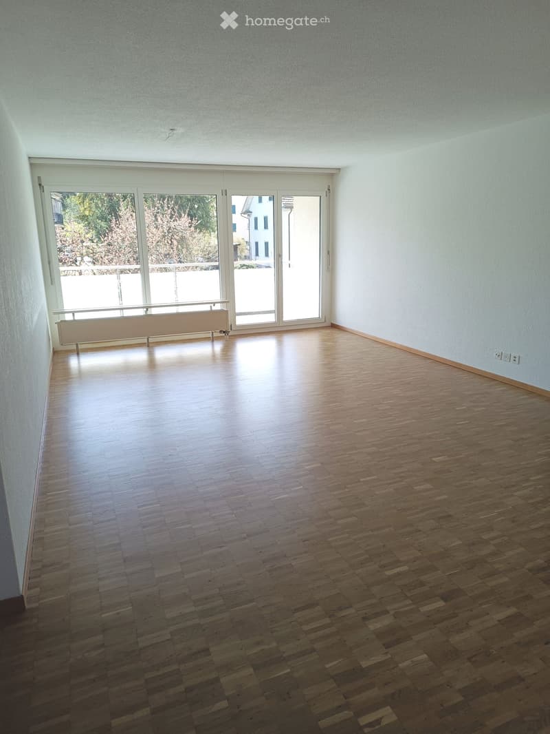 Empty room with wooden flooring, large sliding glass doors leading to a balcony, and light blue walls.