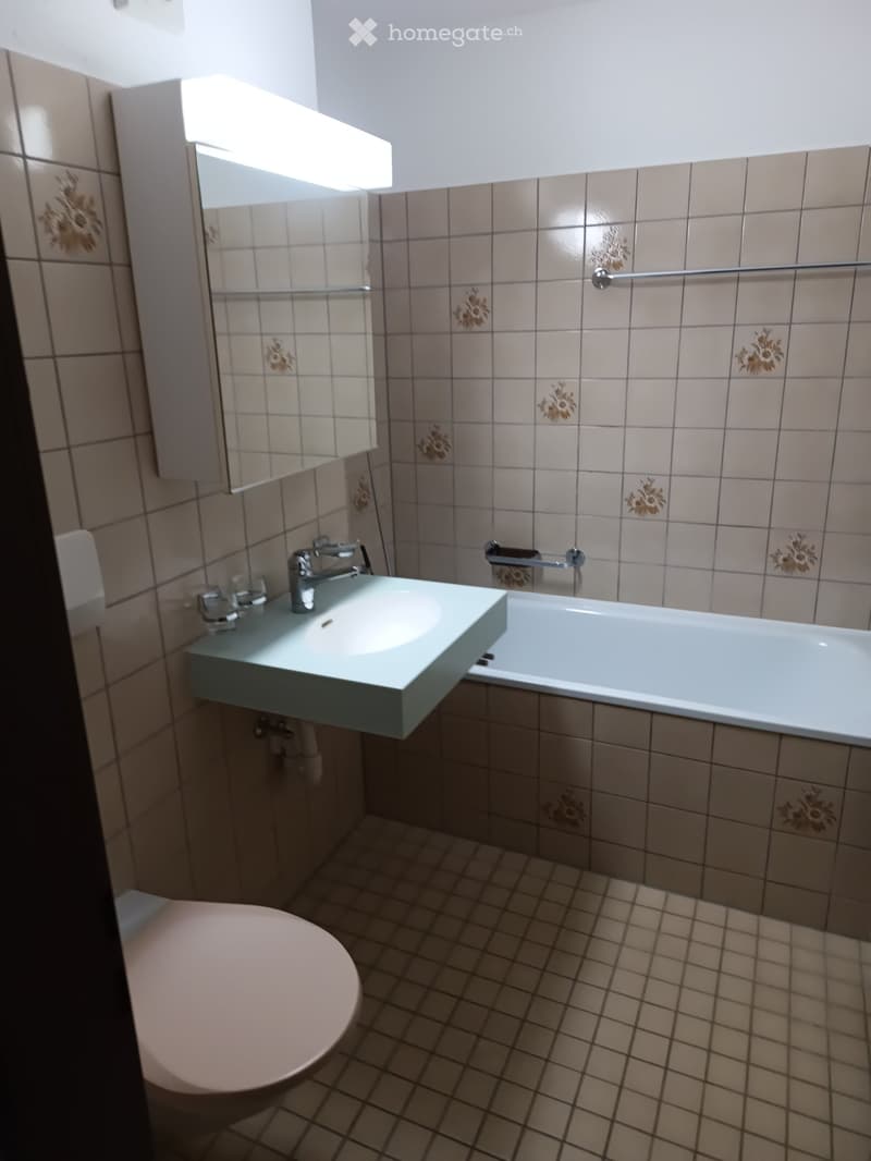Bathroom with beige tiled walls and floor, featuring a sink with a faucet, a bathtub, a toilet, a mirror with a cabinet, and a towel rack.