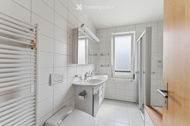 Modern bathroom with white tiles, a sink, toilet, mirror, radiator, and a glass-enclosed shower area.