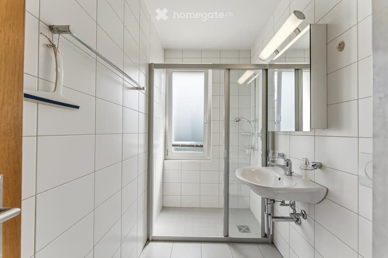 Modern bathroom with white tiles, a sink with a modern faucet, a large mirror, and a glass-enclosed shower area.