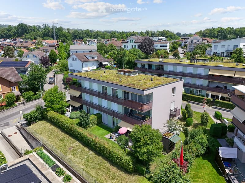 Aerial view of a residential area with multiple buildings, green spaces, and a rooftop garden on one of the structures.