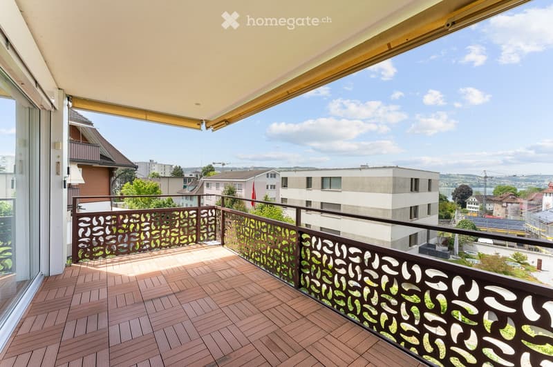 Balcony with wooden decking, decorative metal railing, and a view of the city and surrounding landscape.