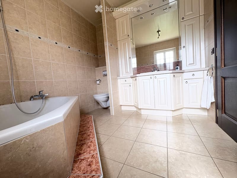 Modern bathroom with beige tiles, a bathtub, toilet, sink, and white cabinets.