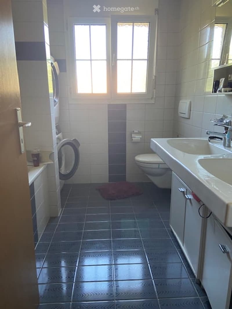 Bathroom with white tiles, dark blue floor tiles, a bathtub, toilet, sink, and a mirror above the sink.