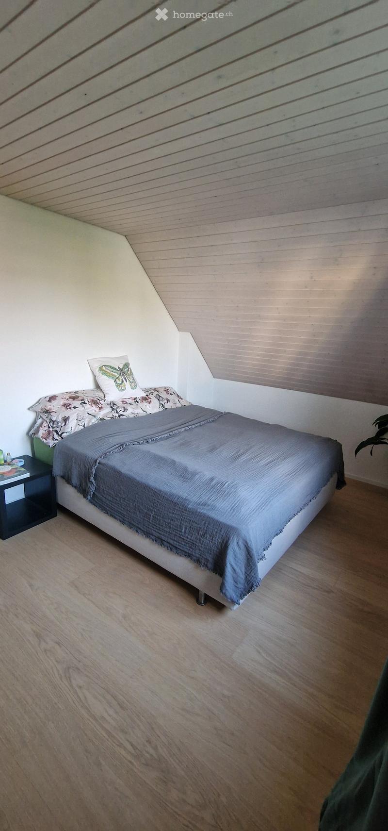 Bedroom with a single bed, grey duvet, floral pillows, and a nightstand with a lamp and books.