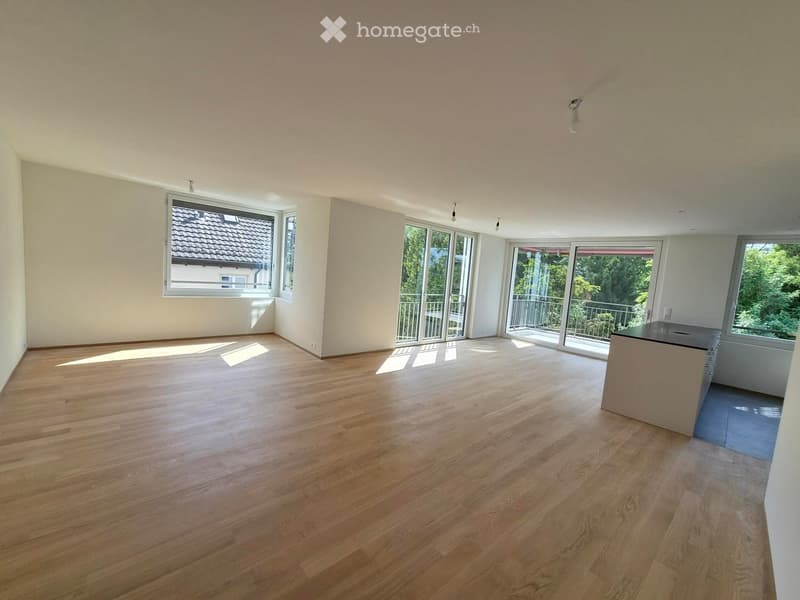Empty room with wooden flooring, large windows, and sliding glass doors leading to a balcony.