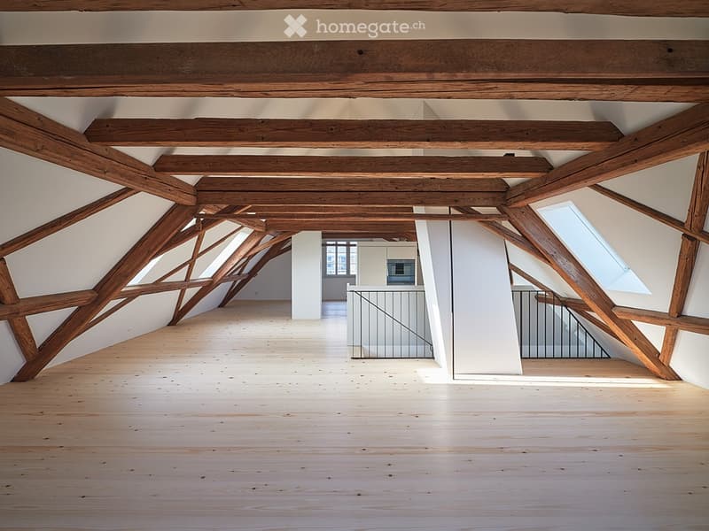 Open, high-ceilinged attic space with exposed wooden beams, wooden flooring, and large skylights. No furniture or equipment visible.