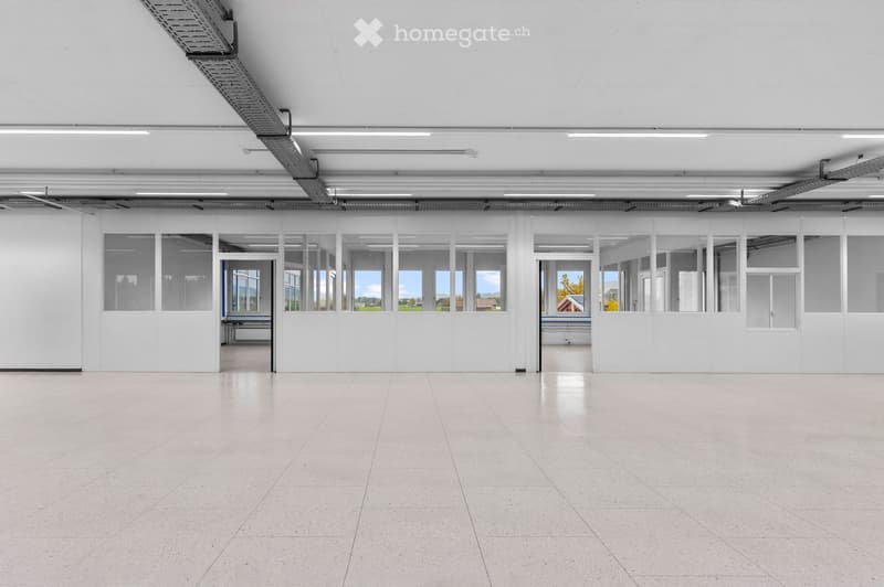 Large, empty room with white walls, a high ceiling, and large glass partitions. The floor is made of light-colored tiles, and the space is well-lit with overhead lighting.
