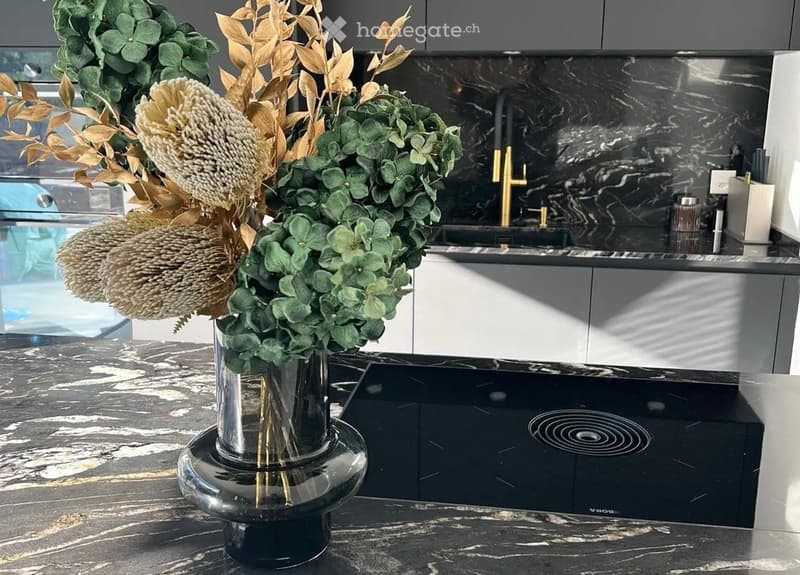 Modern kitchen with dark marble countertops, sleek grey cabinets, and a central island with a decorative flower arrangement.