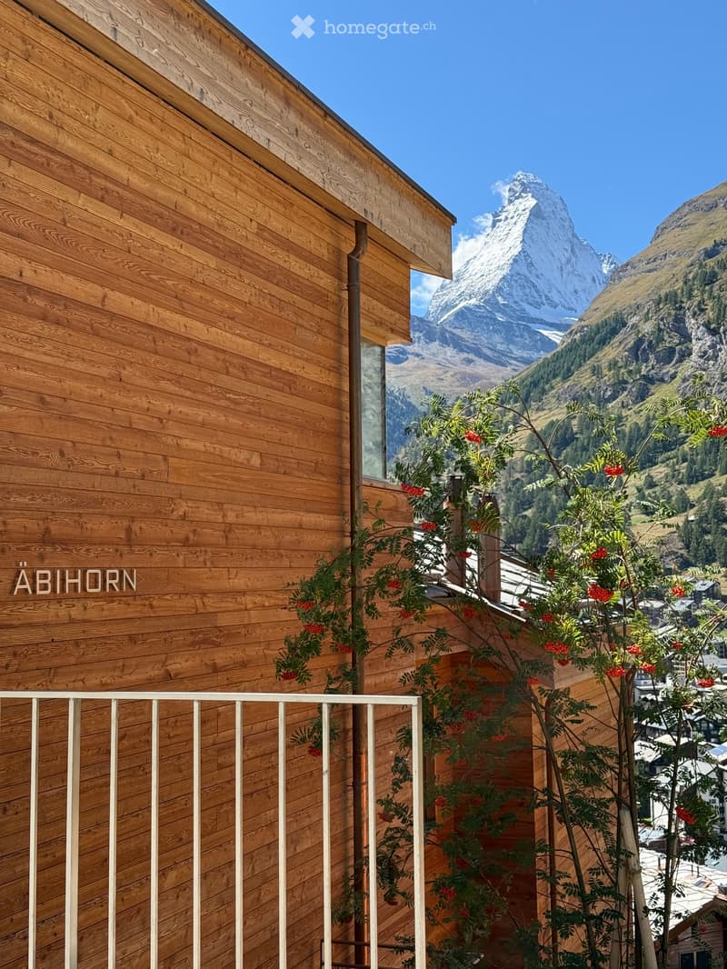 Wooden building exterior with a balcony, featuring a view of snow-capped mountains and a town below.
