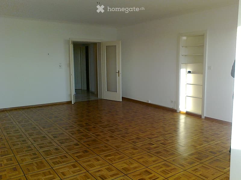 Empty room with wooden flooring, white walls, and open doors leading to other spaces.