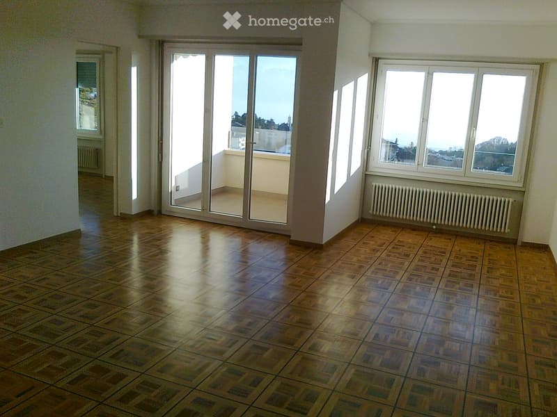 Empty room with wooden flooring, large windows, and a sliding glass door leading to a balcony.