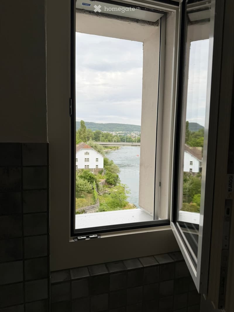 Empty room with large windows offering a scenic view of a river and surrounding landscape.