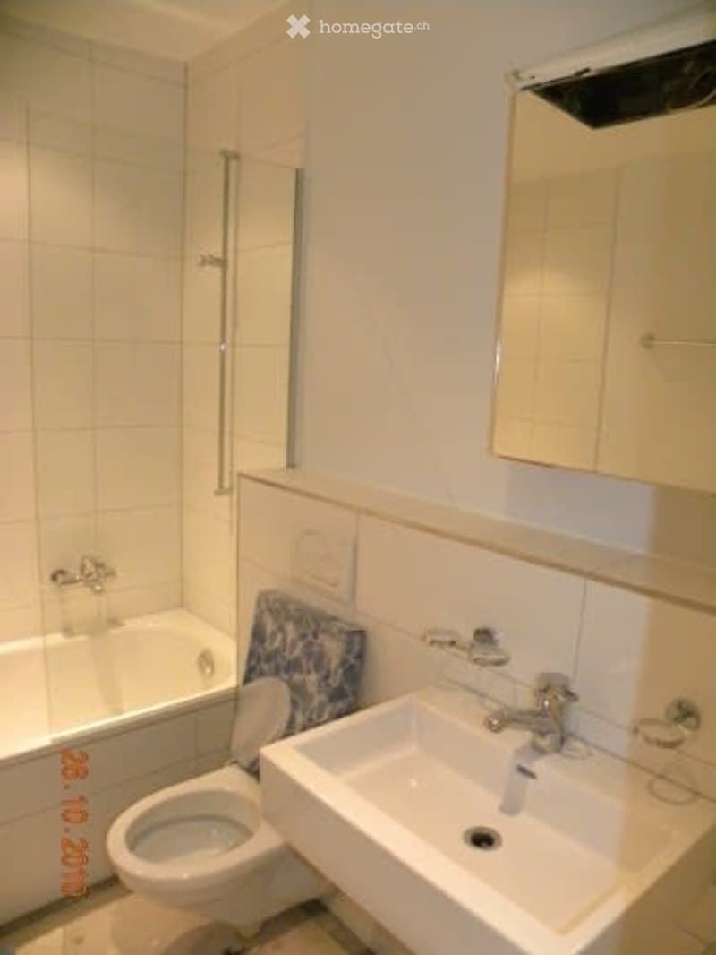 Modern bathroom with white tiles, a bathtub, toilet, sink, and a mirror above the sink.