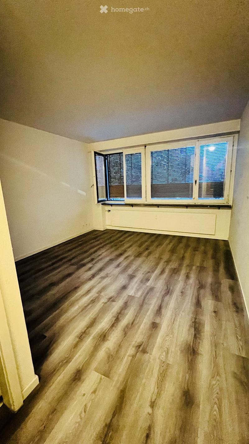 Empty room with wooden flooring, white walls, and large windows with blinds. No furniture or equipment present.