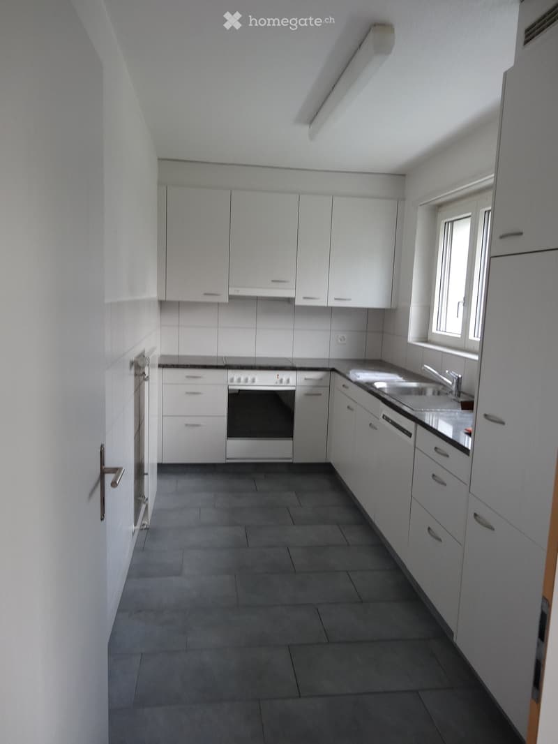 Empty kitchen with white cabinets, stainless steel appliances, and dark tiled floor.