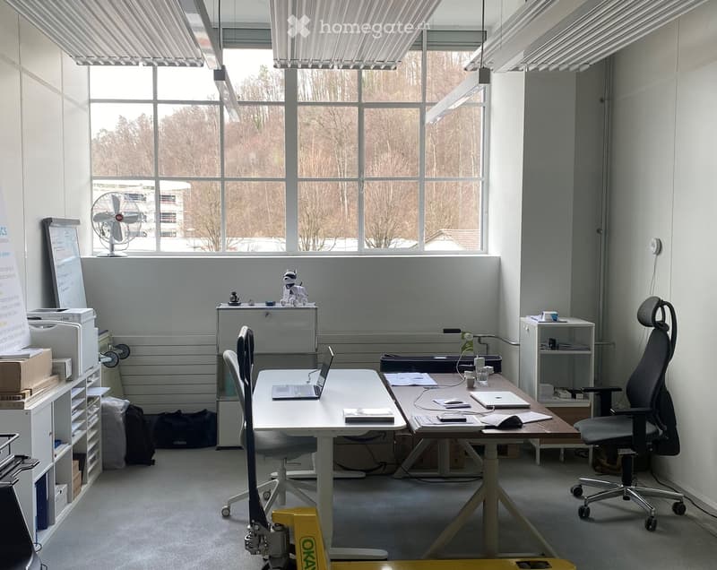 Office space with two desks, chairs, laptops, a fan, a refrigerator, and a screen on the wall.