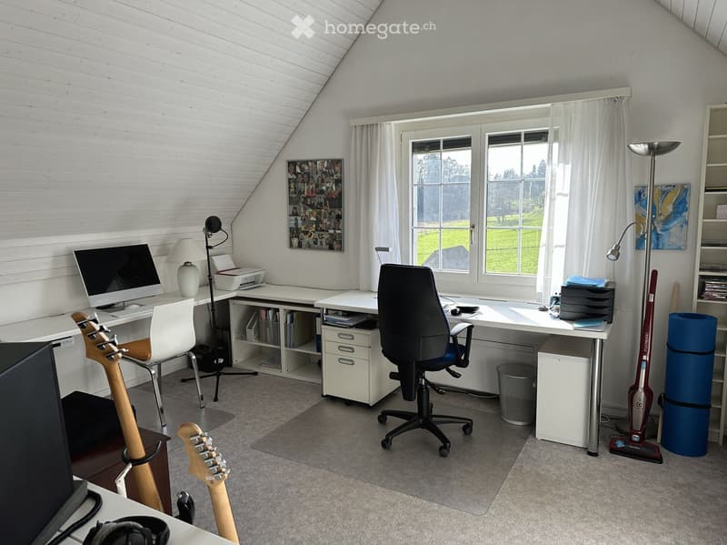 A room with a desk, computer, chair, lamp, printer, guitar, and other office equipment.