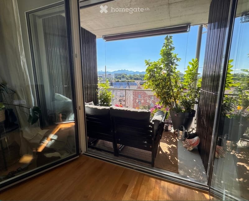 Balcony with a sofa, chair, potted plants, and a scenic city view.