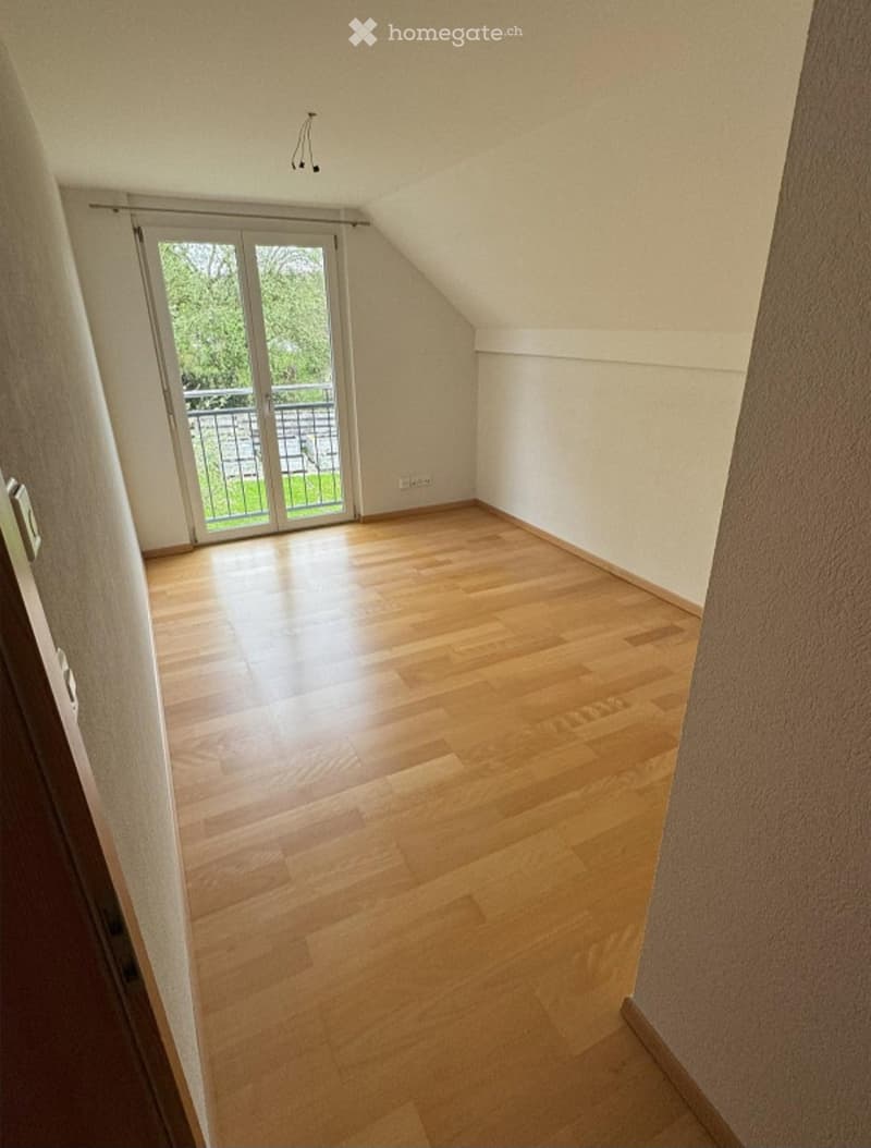 Empty room with wooden flooring, white walls, and a sliding glass door leading to a balcony.