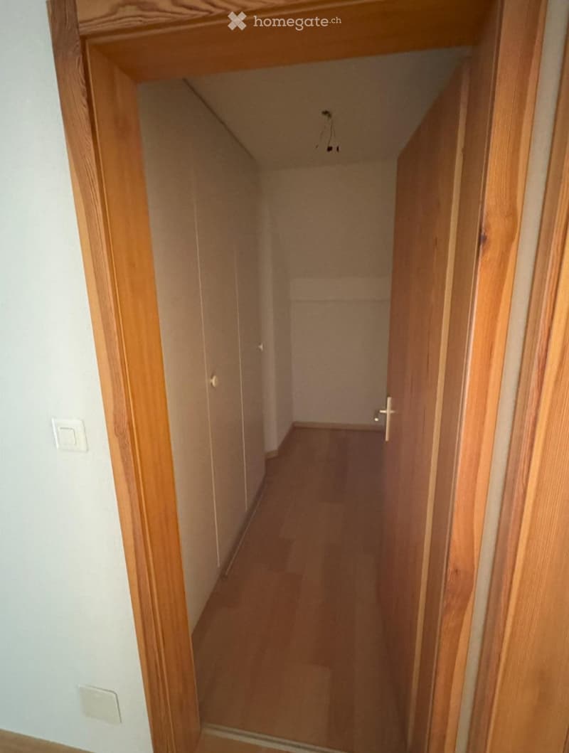 Empty hallway with wooden flooring and white walls, featuring a visible electrical outlet and a partially open door at the end.