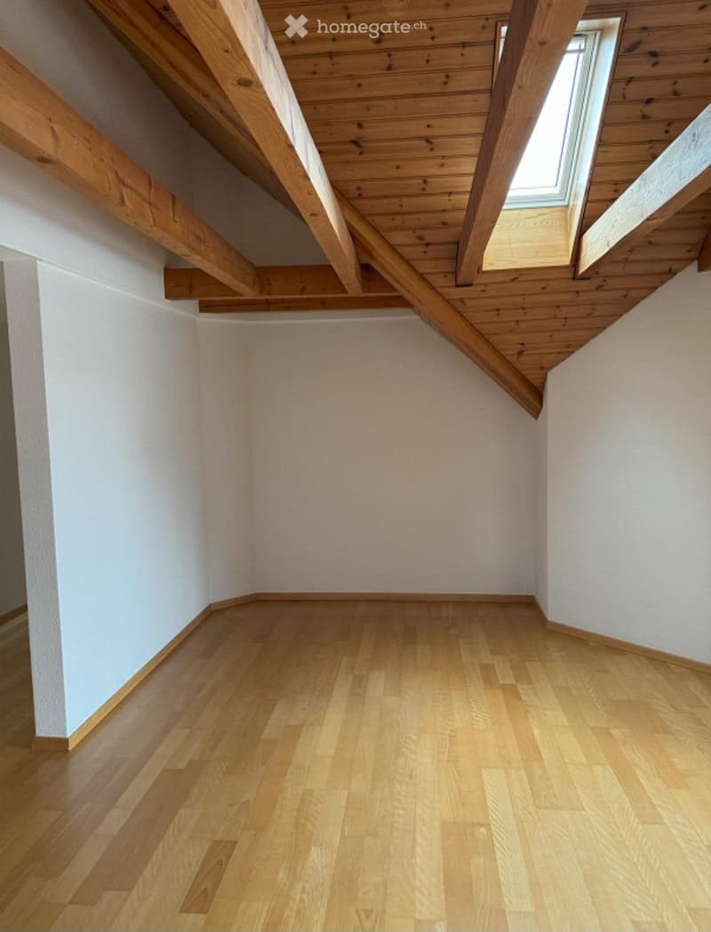 Empty room with wooden flooring and white walls, featuring exposed wooden beams and skylight windows on the sloped ceiling.