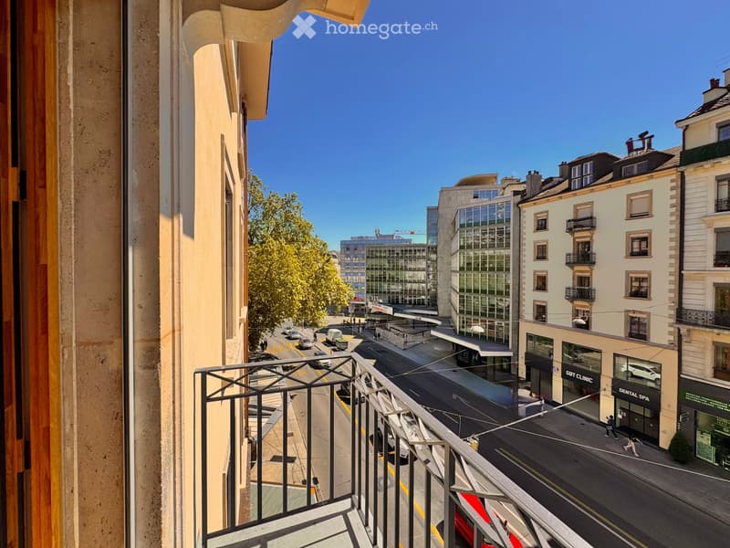 Balcony overlooking a city street with modern buildings, shops, and a clear blue sky.