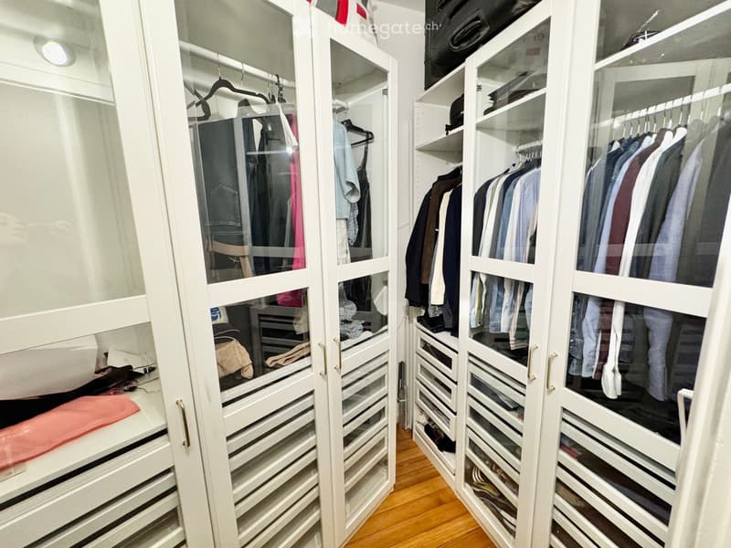 A spacious, well-organized walk-in closet with white built-in wardrobes and drawers, filled with neatly arranged clothing and accessories.