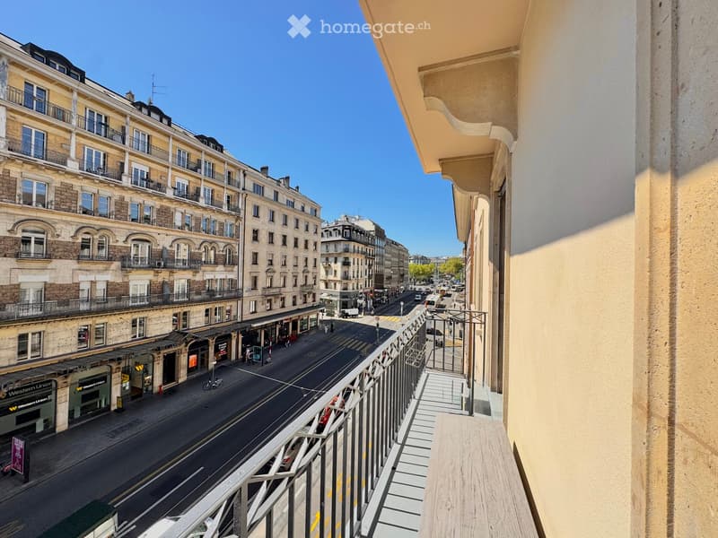Balcony overlooking a quiet urban street lined with classic European buildings, featuring metal railings and wooden flooring.