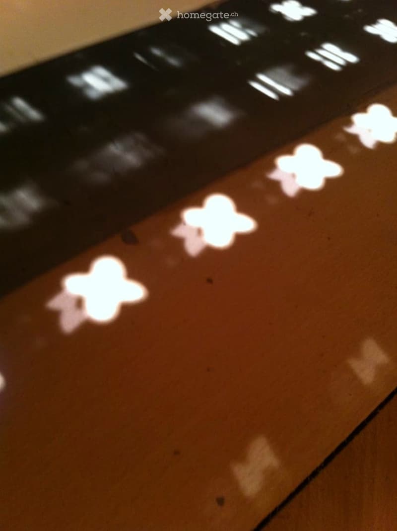 A close-up of a black remote control with illuminated buttons and a wooden surface beneath it.