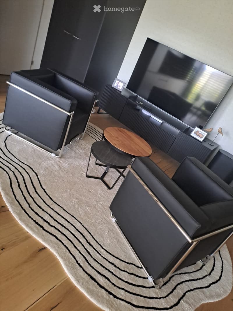 Modern living room with a large television, black leather sofa, wooden coffee table, and decorative items.
