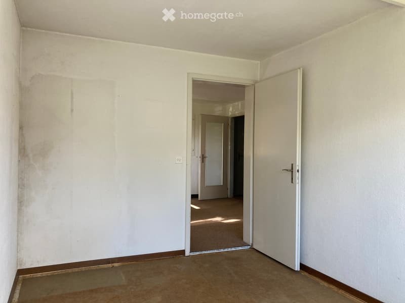 an empty room with white walls, brown carpet floor, two doors, one leading to another room