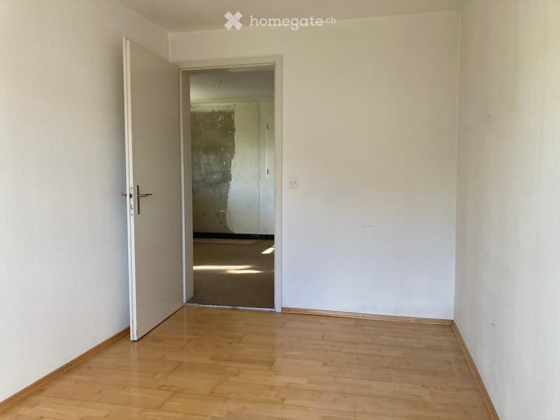 An empty room with an open door and a hallway leading to a larger room