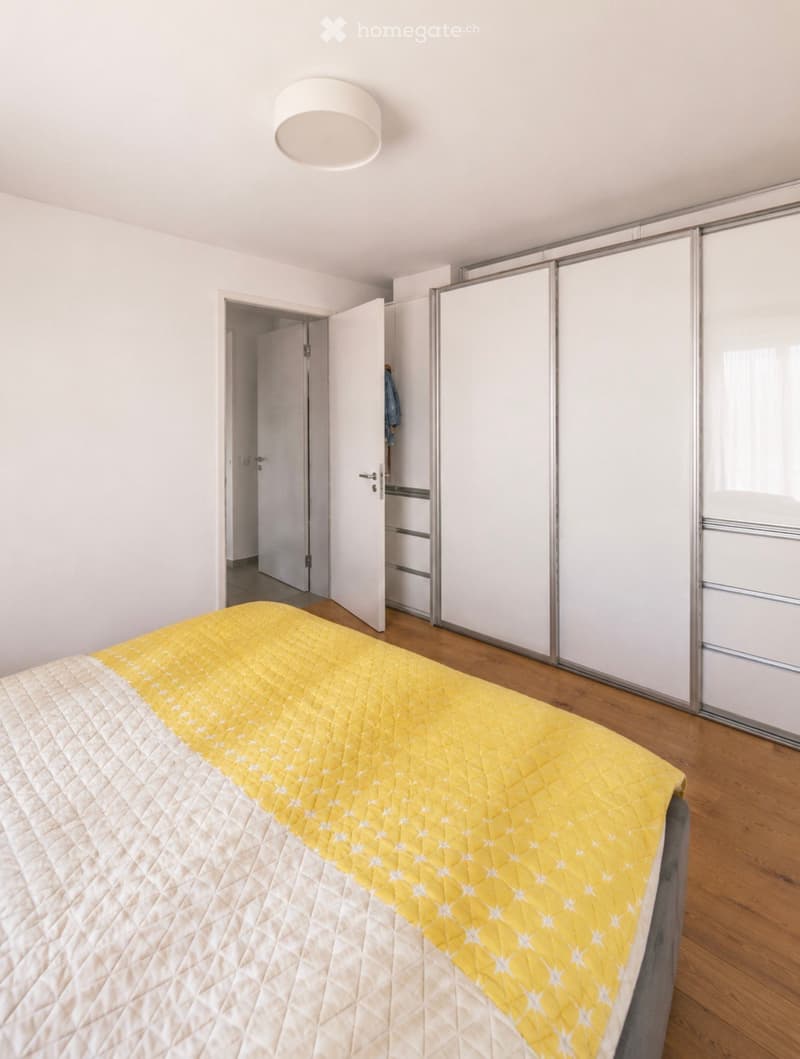 Modern bedroom with a yellow and white quilted bedspread, wooden flooring, and a large sliding wardrobe with mirrored doors.