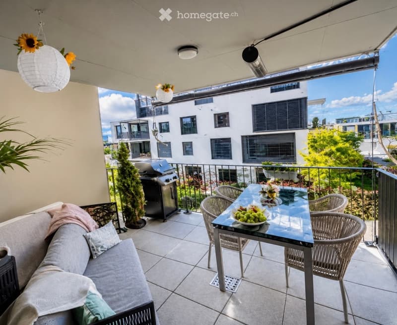 Balcony with a sofa, glass table, wicker chairs, grill, and decorative bowl of fruit.