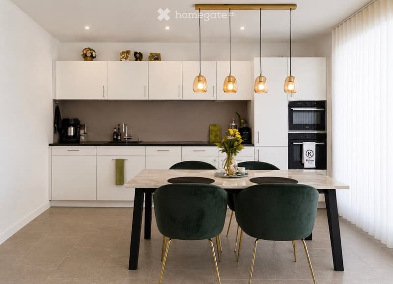 Modern kitchen with white cabinets, a central island, and a dining area featuring a marble table and green velvet chairs.