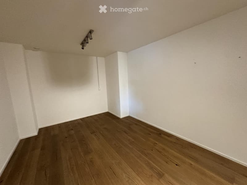 Empty room with wooden flooring and white walls, featuring a ceiling light fixture.
