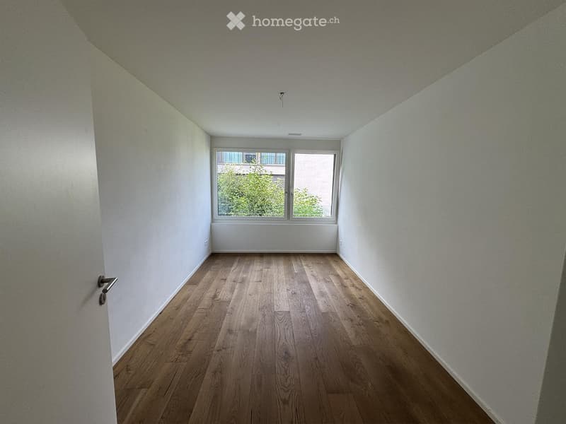 Empty room with wooden flooring and white walls, featuring a window with a view of greenery outside.