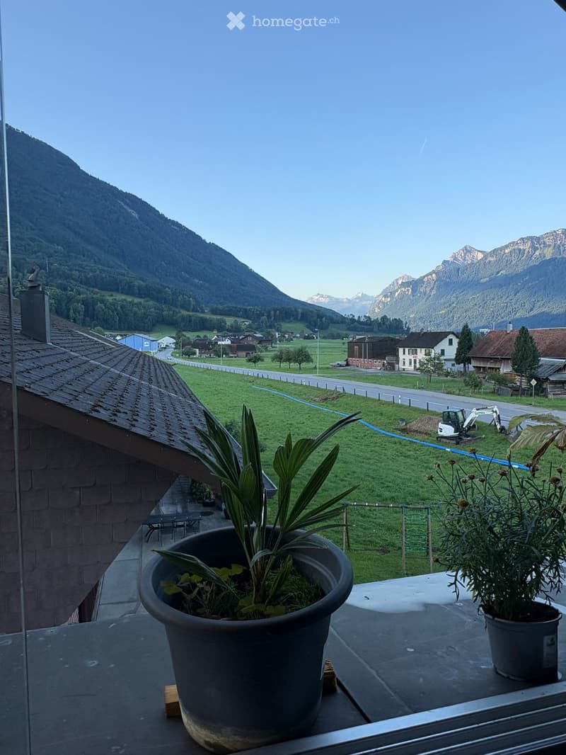 Balcony with a scenic mountain view, featuring a table, chairs, and potted plants.