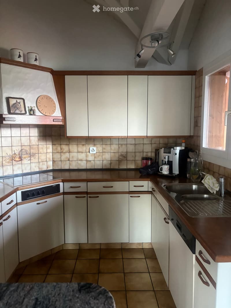 A compact kitchen with white cabinets, wooden countertops, and tiled backsplash. Features include a sink, coffee maker, oven, and various small appliances.