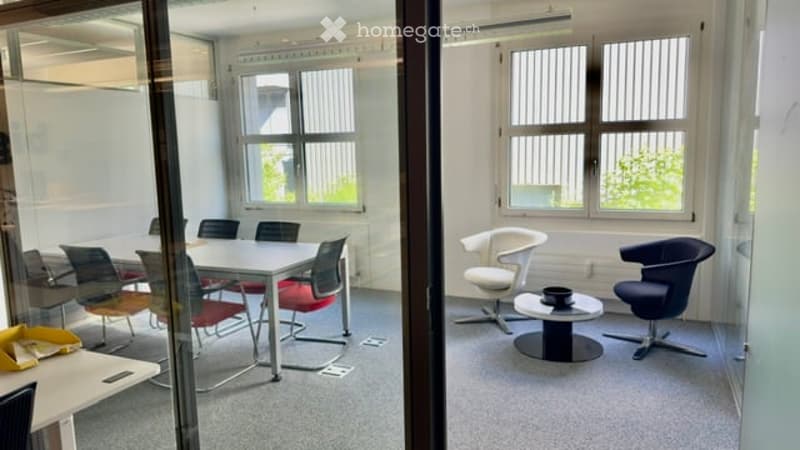 Modern office space with a meeting table, chairs, and a small seating area with a stool and cup.