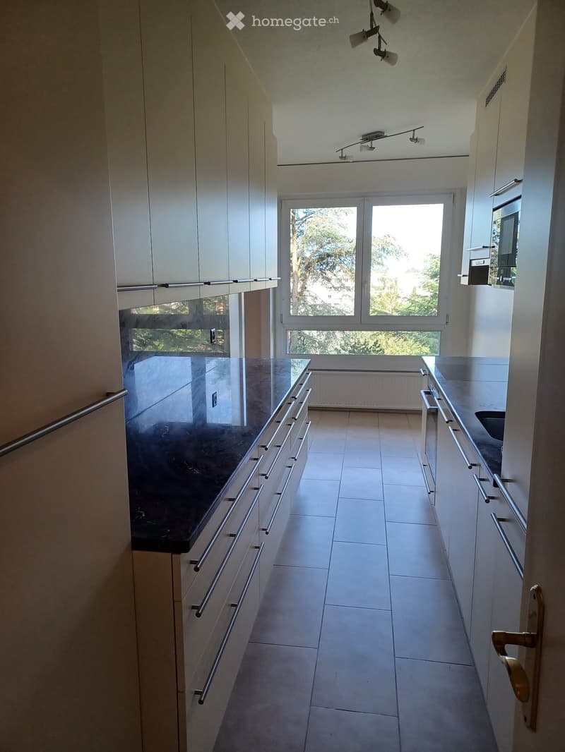 Modern hallway with white tiled flooring, white walls, and built-in cabinets with silver handles. Features a large window at the end, allowing natural light to enter.