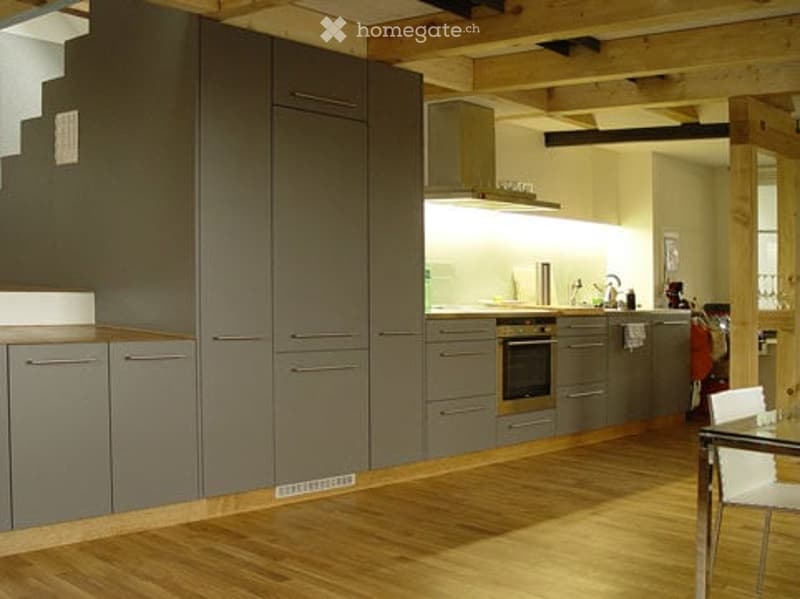 Modern kitchen with grey cabinets, stainless steel appliances, wooden flooring, and a white chair near the dining area.