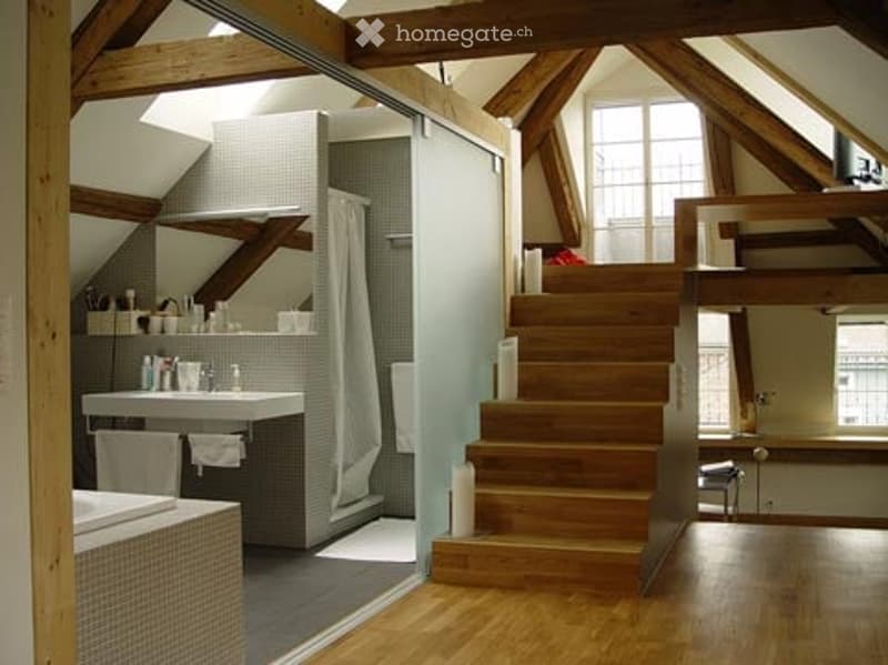 Modern bathroom with wooden beams, large window, sink, mirror, towel, bathtub, and wooden staircase leading to another level.