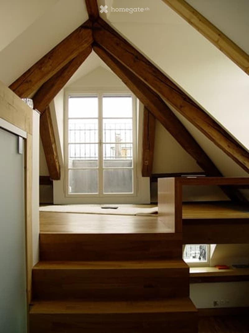 Attic hallway with wooden beams, skylight window, and wooden staircase leading up.