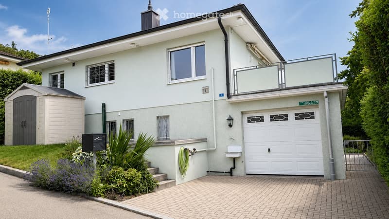 Two-story house with white exterior, garage, balcony, and garden area with plants and a mailbox.